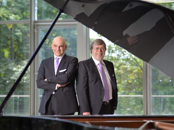 A photo of the piano duo Anagnoson and Kinton, posing by a grand piano.